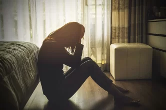 Mujer con depresión causada por trauma migratorio sentada en el suelo de su habitación