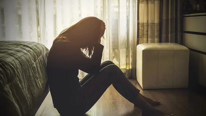 Mujer con depresión causada por trauma migratorio sentada en el suelo de su habitación