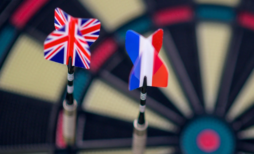 Dardos con banderas de Reino Unido y Francia en una diana.
