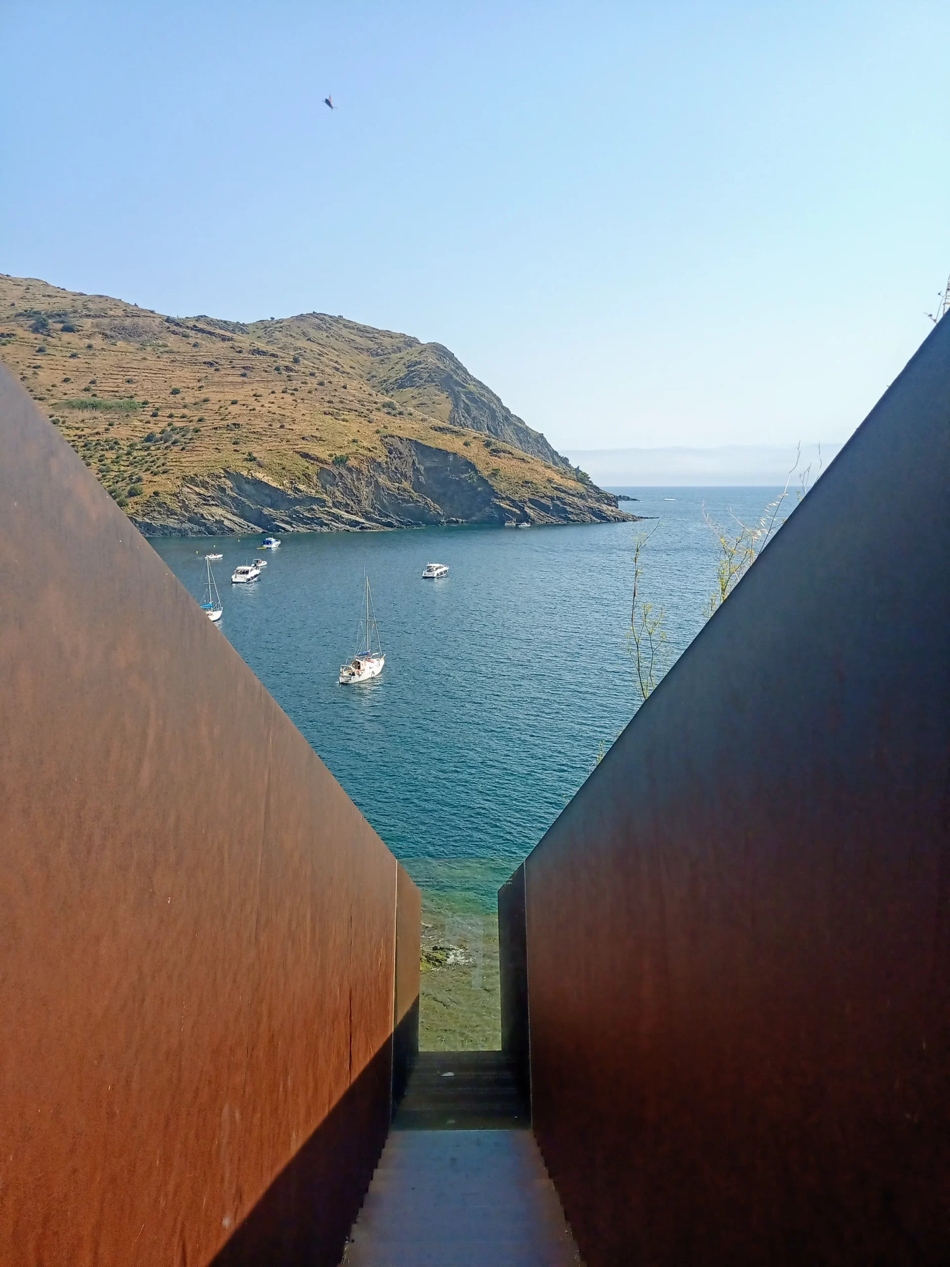 Escaleras que descienden hacia el mar en Portbou, Girona, con vista a las montañas y veleros