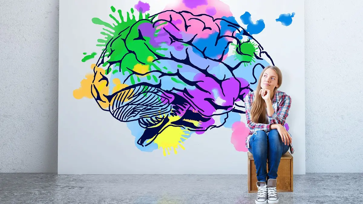 Mujer observando una ilustración colorida de un cerebro que representa la creatividad.