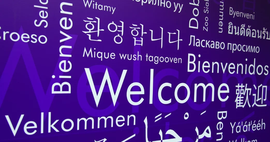 Palabras de bienvenida en distintos idiomas sobre fondo violeta simbolizan la diversidad lingüística global.
