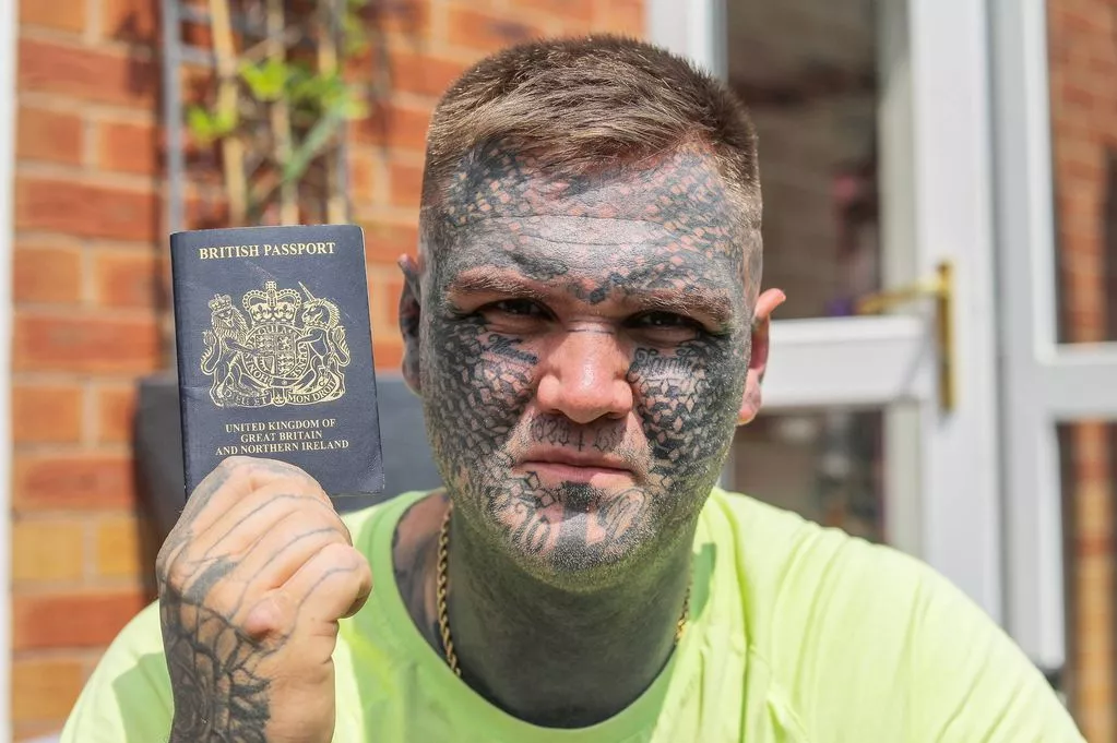 Hombre británico con rostro tatuado sostiene su pasaporte.