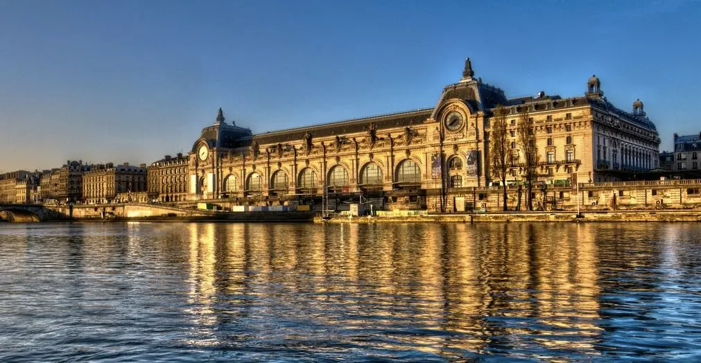 Vista exterior del Museo de Orsay en París con su arquitectura Beaux Arts y reflejo en el Sena.