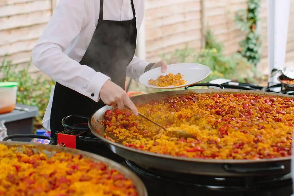 Chef sirviendo paella valenciana en evento gastronómico.