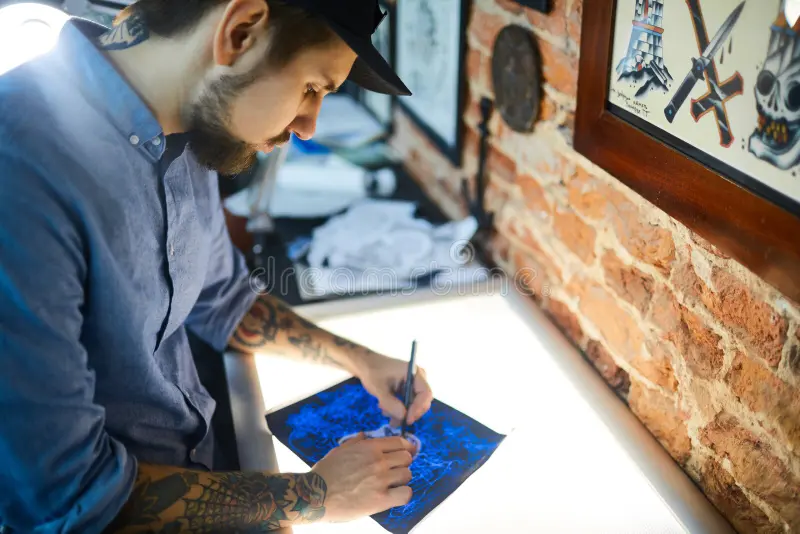 Artista del tatuaje preparando un diseño sobre mesa de luz.
