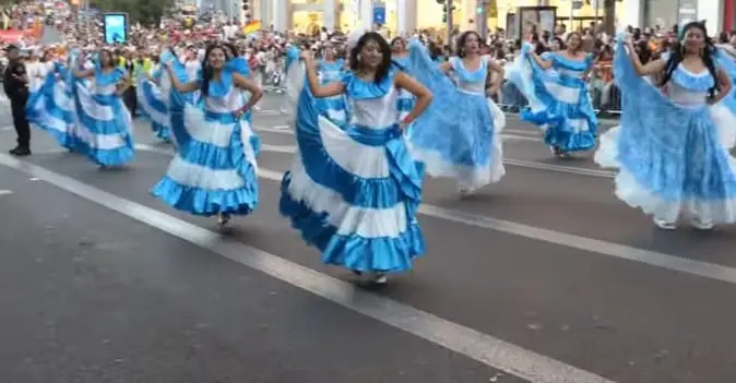 Bailarinas con vestidos celestes y blancos desfilan por la Gran Vía en la Cabalgata de la Hispanidad 2025.