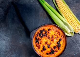 Pastel de choclo chileno acompañado de mazorcas de maíz fresco sobre fondo oscuro