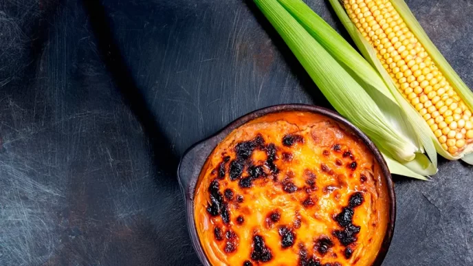 Pastel de choclo chileno acompañado de mazorcas de maíz fresco sobre fondo oscuro
