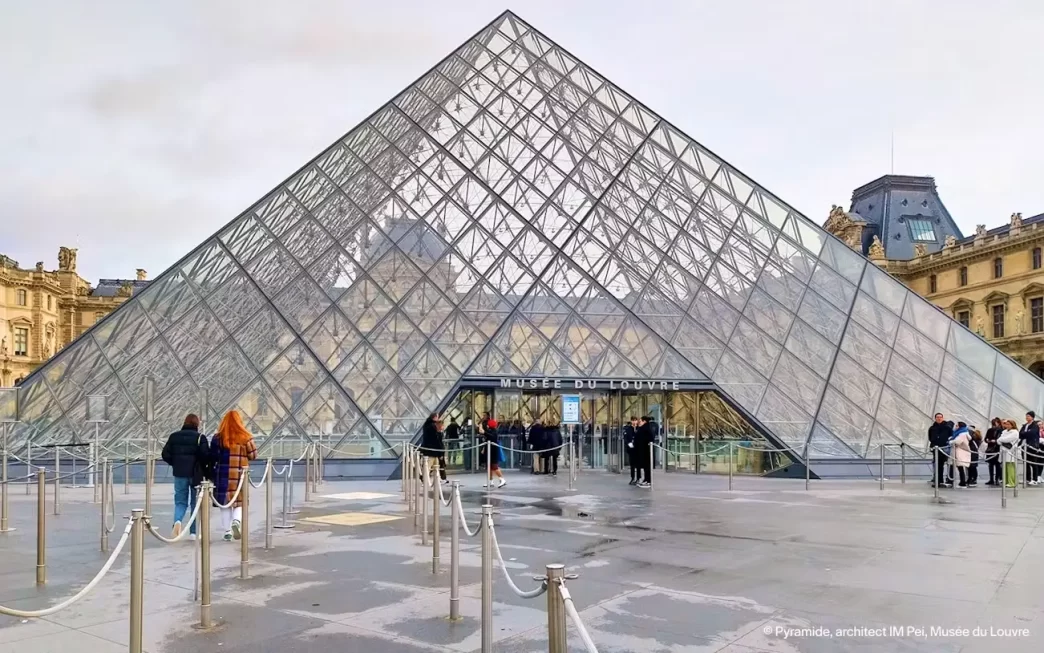 Entrada principal del Museo del Louvre en París con visitantes frente a la pirámide de cristal.