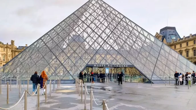 Entrada principal del Museo del Louvre en París con visitantes frente a la pirámide de cristal.