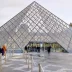 Entrada principal del Museo del Louvre en París con visitantes frente a la pirámide de cristal.