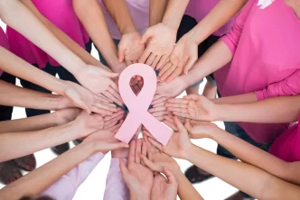 Manos unidas alrededor de un lazo rosa símbolo del cáncer de mama.