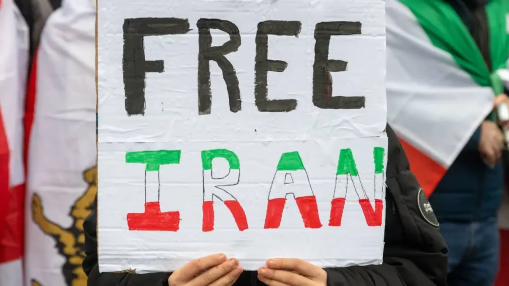 Protestas por la crisis en Irán con manifestantes sosteniendo un cartel de “Free Iran”.