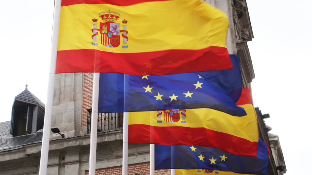 Regularización migrantes España en contexto del debate migratorio europeo con banderas de España y la Unión Europea.