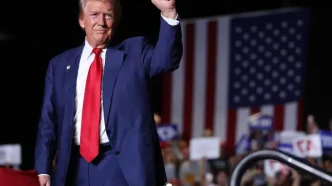 : Donald Trump saludando durante un mitin político ante una bandera de Estados Unidos.