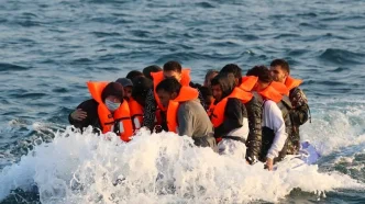 Un grupo de migrantes con chalecos salvavidas naranjas cruzando el Canal de la Mancha en una pequeña lancha.