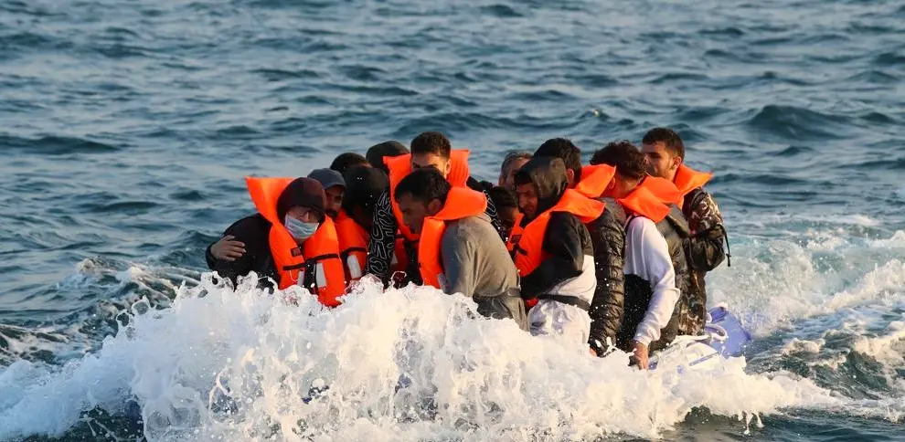Un grupo de migrantes con chalecos salvavidas naranjas cruzando el Canal de la Mancha en una pequeña lancha.