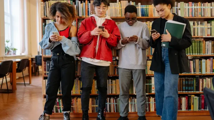 Cuatro jóvenes mirando sus teléfonos móviles en una biblioteca.