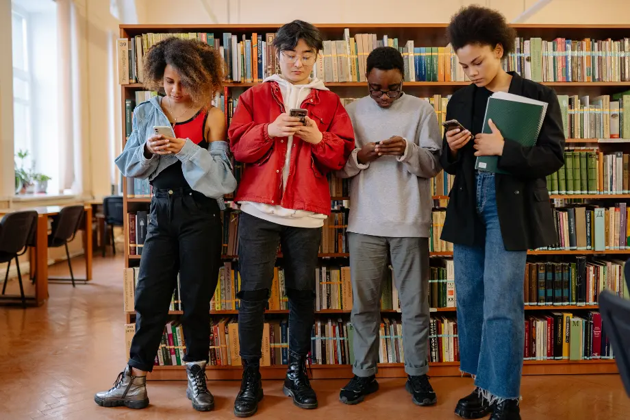 Cuatro jóvenes mirando sus teléfonos móviles en una biblioteca.