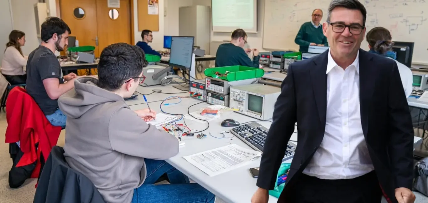 Andy Burnham sonriente en un aula técnica junto a jóvenes estudiantes.