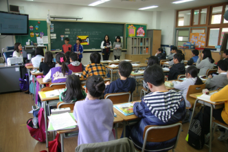 Interior de una aula de escuela primaria con estudiantes sentados en escritorios mirando hacia la parte delantera de la clase.
