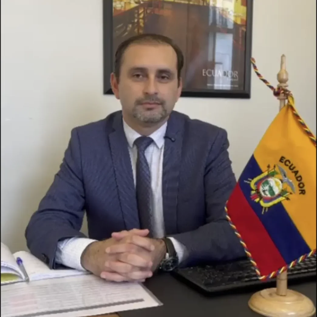 El Cónsul Christian Valencia sentado en su despacho de la Sección Consular de la Embajada del Ecuador en París junto a la bandera del país.