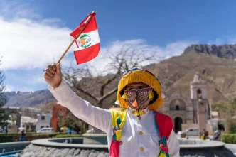 Persona con indumentaria tradicional y máscara sosteniendo una pequeña bandera de Perú durante las celebraciones.