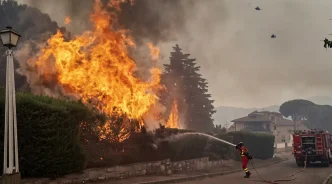Bombero extinguiendo las llamas de un incendio forestal en una zona residencial de España con apoyo aéreo.