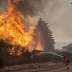 Bombero extinguiendo las llamas de un incendio forestal en una zona residencial de España con apoyo aéreo.