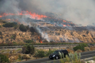 Un vehículo circula por una carretera cercana a un incendio forestal activo en el sur de España.