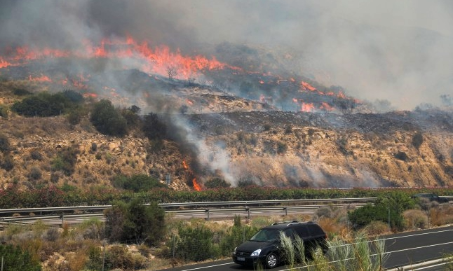 Un vehículo circula por una carretera cercana a un incendio forestal activo en el sur de España.