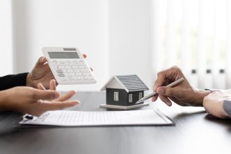 Dos personas analizando un contrato inmobiliario junto a una calculadora y una figura de una casa en miniatura.