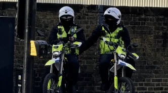 Dos agentes de policía británicos patrullando equipados con cascos y motocicletas en una calle urbana