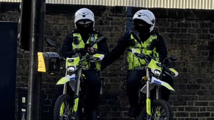 Dos agentes de policía británicos patrullando equipados con cascos y motocicletas en una calle urbana
