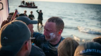 El nadador Bartłomiej Kubkowski emocionado en la playa tras completar su hazaña contra el cáncer.