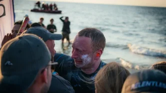 El nadador Bartłomiej Kubkowski emocionado en la playa tras completar su hazaña contra el cáncer.