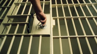 Mano abriendo la cerradura de unos barrotes de prisión con unas llaves