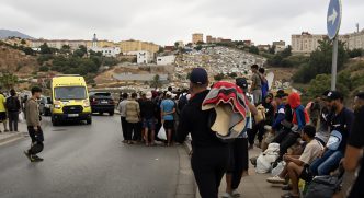 Grupo de migrantes y una ambulancia en una carretera tras la llegada masiva a Ceuta