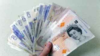 Mano sosteniendo billetes de libras esterlinas en representación de las ayudas sociales