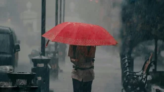 Una persona camina bajo la lluvia intensa protegiéndose con un paraguas rojo en la calle