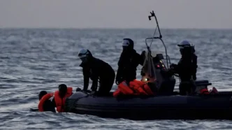 Equipos de rescate y seguridad operando en una pequeña embarcación con migrantes en alta mar.