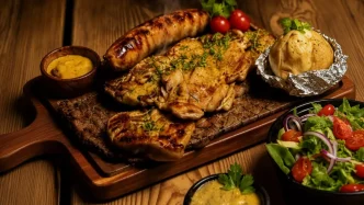 Tabla de madera con una parrillada mixta latinoamericana, chorizo, papas asadas y ensalada fresca