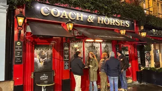 Clientes de pie charlando en la entrada de un tradicional pub iluminado en Londres