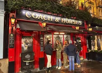 Clientes de pie charlando en la entrada de un tradicional pub iluminado en Londres
