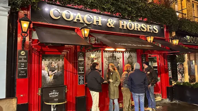 Clientes de pie charlando en la entrada de un tradicional pub iluminado en Londres