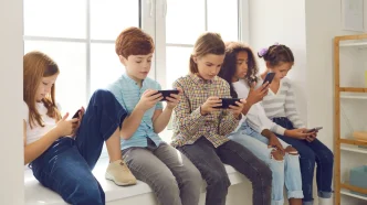 Niños y niñas sentados utilizando teléfonos móviles en el colegio