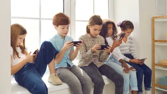 Niños y niñas sentados utilizando teléfonos móviles en el colegio