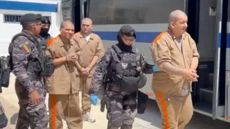 Reclusos rapados y uniformados esposados en parejas durante un operativo de traslado carcelario
