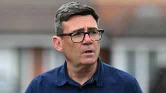 Retrato del primer ministro británico Andy Burnham con gafas y camisa azul.